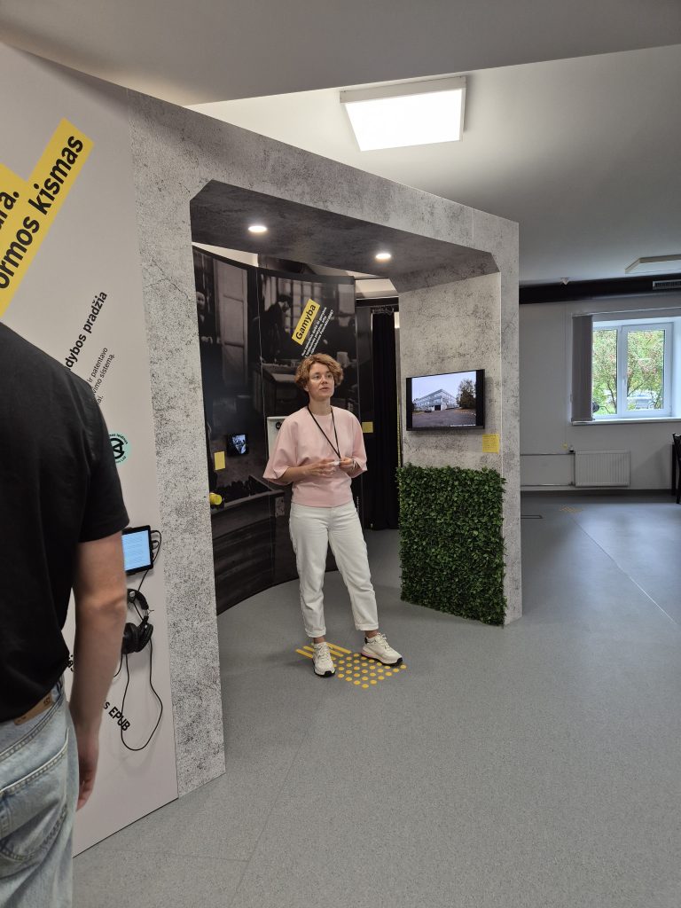 A guide stands in the exhibition area in front of an arch with display panels and a screen.